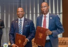 Sierra Leone and Senegal Seal Landmark Mining and Energy Treaty to Boost Regional Cooperation Two men in business suits hold brown folders with a tree emblem during a formal signing ceremony indoors.