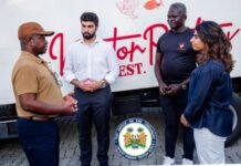 From Poultry to Fish Farming: President Bio Champions Local Production and Private Sector Investment Four people in a discussion in front of a bus with red lettering; a presidential seal sits on the ground between them.