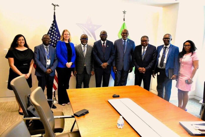 Group of ten professionals in business attire posing for a photo in a conference room with flags behind them (U.S. flag and another flag).