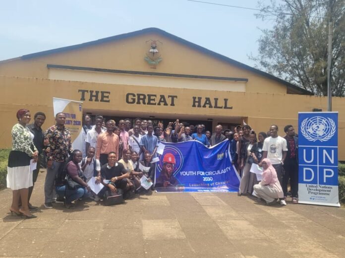 A large group of people posing for a group photo in front of a building labeled 'THE GREAT HALL', with a UNDP banner on the right and a blue 'Youth for Circularity 2030' banner in the center.