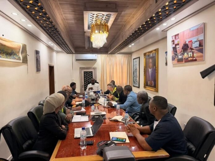 Diverse team of professionals in a conference room, discussing around a long wooden table with laptops and water bottles.