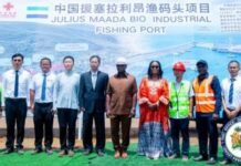 $55 Million Fishing Port Initiative Unveiled, Signals New Era for Sierra Leone’s Maritime Development Group of officials and workers standing in front of a banner for the Julius Maada Bio Industrial Fishing Port at a port site.