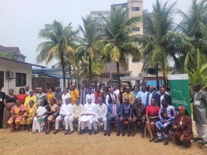 Large group of people posing for a photo outdoors, seated and standing in front of palm trees and a building, suggesting a community or conference event.
