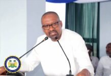 Vice President Hands Over Staff Bus to Koidu Government Hospital to Boost Healthcare Delivery Man in white shirt speaks at a podium with two microphones; official seal visible on the lectern.