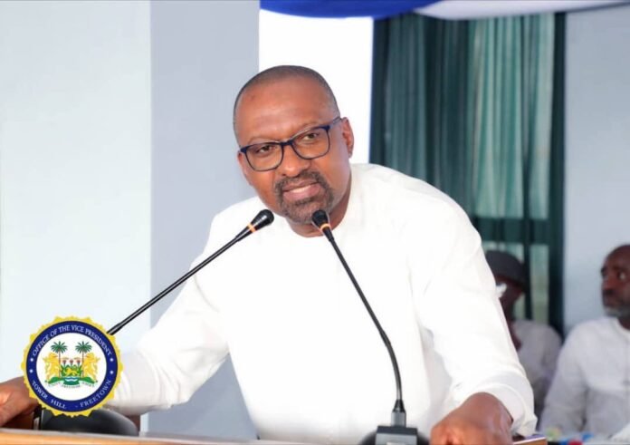 Man in white shirt speaks at a podium with two microphones; official seal visible on the lectern.