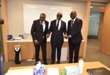 World Bank, IMF Laud Finance Minister for the Impressive Country’s Macroeconomic Performance Three men in suits shake hands and smile in a corporate office, standing in front of a counter with supplies and a whiteboard behind them.