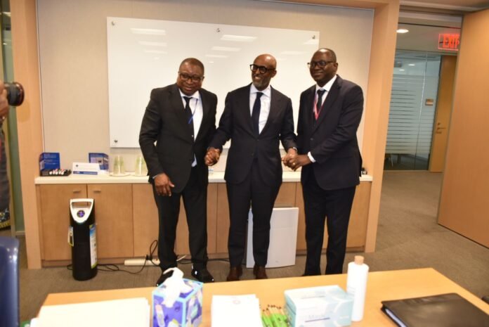Three men in suits shake hands and smile in a corporate office, standing in front of a counter with supplies and a whiteboard behind them.