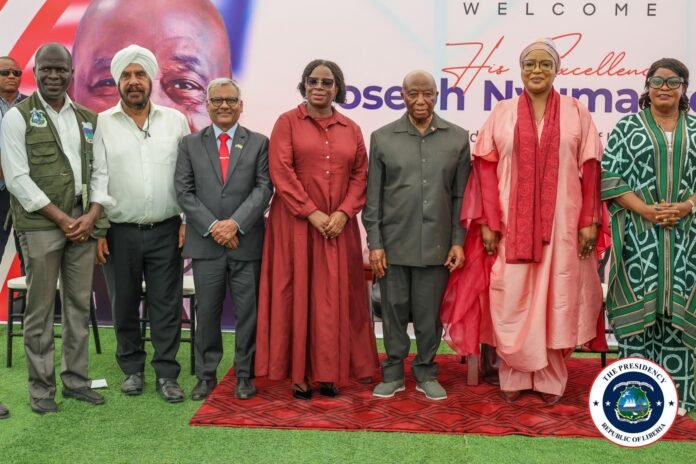 Group of seven dignitaries posing on a red carpet at a welcome event, with a banner and the Liberian presidential seal visible.