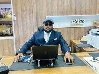 SLPHA Strengthens Controls in Support of National Fight Against Drugs A man in a blue suit and flat cap sits at a wooden desk with a laptop, in a tidy office environment.