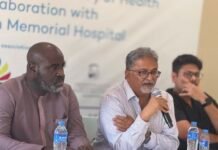 Choithram Rolls Out 2026 Free Cataract Outreach Targeting 3,000 Beneficiaries Nationwide Panel of three men at a conference table; center man speaks into a microphone while others listen, with water bottles on the table and a blurred banner in the background.