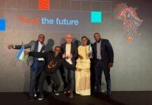 Orange Middle East and Africa Unveils Bold ‘Trust the Future’ Plan for 2026–2030 Expansion Six diverse adults posing on a stage in front of a backdrop reading 'Trust the future' with a colorful fingerprint graphic, some holding small flags and smiling.