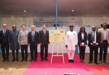 From Classroom to Career: ‘Excellence Skills Academy’ Transforms Youth Prospects Group of formally dressed people standing on a pink carpet during an unveiling ceremony, with a signboard on an easel at the center and a banner in the background.