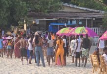 CODE Hosts Annual Student Outing at Number 2 River to Boost Networking and Mental Wellness Crowd of people in swimsuits standing and chatting on a sunny beach near colorful umbrellas and outdoor seating.