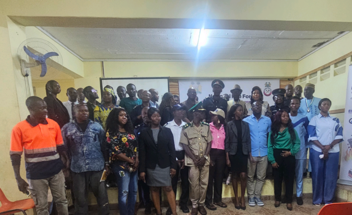 Group photo of a diverse crowd in uniforms and casual attire posing in a hall with a banner in the background.