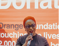 Orange Foundation Opens Call for Digital Skills Trainers Under ‘Threads of Hope’ Programme Woman in an orange hijab speaks into a microphone at a podium on an orange foundation backdrop.