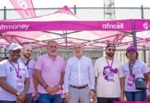 Africell & NBA Africa Host Junior Basketball Clinic for Over 350 Young Athletes in Freetown Six people pose for a group photo under a pink Africell promotional tent at an outdoor event, wearing lanyards and casual clothes.