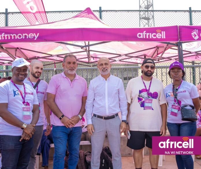 Six people pose for a group photo under a pink Africell promotional tent at an outdoor event, wearing lanyards and casual clothes.