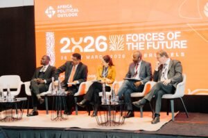 Five panelists in suits seated on a stage, discussing at the Africa Political Outlook 2026 conference on a bright orange backdrop in the background.
