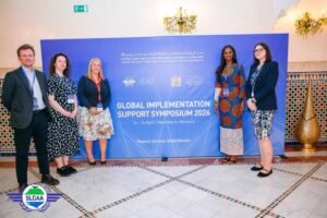 Group of five professionals posing beside a blue banner for the Global Implementation Support Symposium 2026 (Marrakech, Morocco). Links ICAO event.