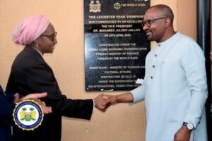 Two officials shake hands in front of a commemorative plaque for the Leicester Peak Viewpoint project, with World Bank involvement evident and a ceremonial seal visible on the left.