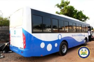 Blue-and-white Ministry of Health staff bus parked on a dirt lot, with a wave design and circular decals along its side, and an official seal in the foreground.