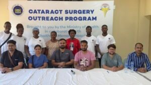 Group of medical staff and volunteers posing in front of a banner reading Cataract Surgery Outreach Program at a health facility.