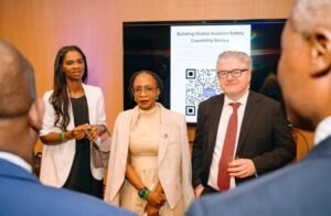 Three professionals posing at a conference in front of a presentation screen showing 'Building Global Aviation Safety Capability Survey' and a QR code, with audience members in the foreground.