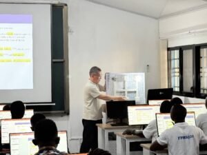 Instructor explaining material to students in a computer lab as a projected slide shows highlighted text lines.