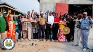 D diverse group of people posing outside a building, holding long loaves of bread aloft in a community ceremony; seal visible in the bottom-left corner.