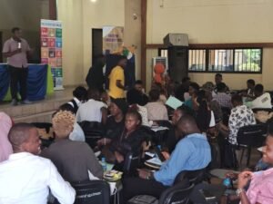 Speaker on a stage addressing a crowded hall with a banner reading Youth for Circularity 2000 in the background.