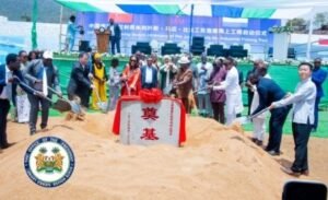 Officials and community members at a groundbreaking ceremony, surrounding a sand mound with shovels and a Chinese-character marker.