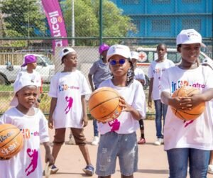 Group of children in white T-shirts with basketballs on an outdoor court, participating in a youth basketball program.