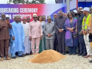 Dignitaries at a groundbreaking ceremony posing behind a sand heap, in front of a colorful banner reading 'Groundbreaking Ceremony'.