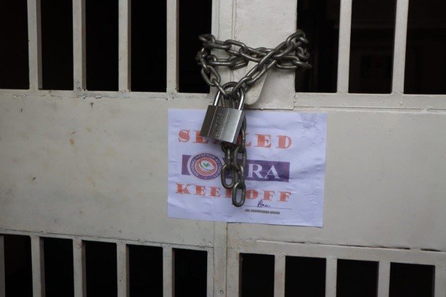 Lock across a metal gate with a heavy chain and padlock; a posted sign reading 'CLOSED' and 'KEEP OFF' behind the bars.