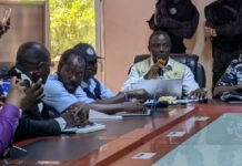 SLPHA Reaffirms Confidence in Port Security as Probe Finds No Cocaine on MV Acronian Man in a beige vest speaks into an orange microphone at a conference table, with colleagues on laptops nearby.
