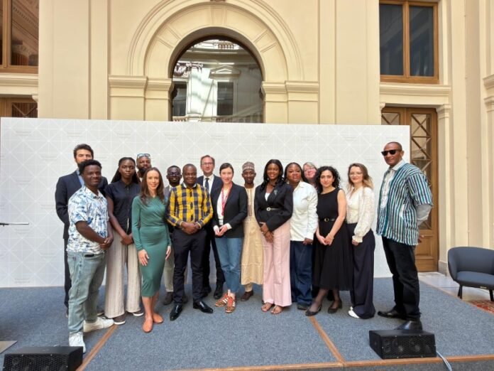 Diverse group of professionals posing on a stage in front of a patterned backdrop at a formal event outside a historic building.