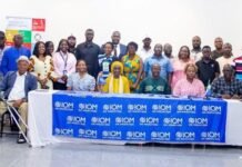Government and IOM Deepen Partnership to Protect Migrant Workers in Sierra Leone Group portrait of diverse officials and participants at an IOM event in Sierra Leone, seated at a table with IOM banners in front.