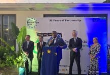 Foreign Minister Hails Enduring EU Sierra Leone Partnership at Europe Day Golden Jubilee Celebration Five people in suits stand on a stage with a blue lectern decorated with EU stars at a Europe Day event titled '50 Years of Partnership.'