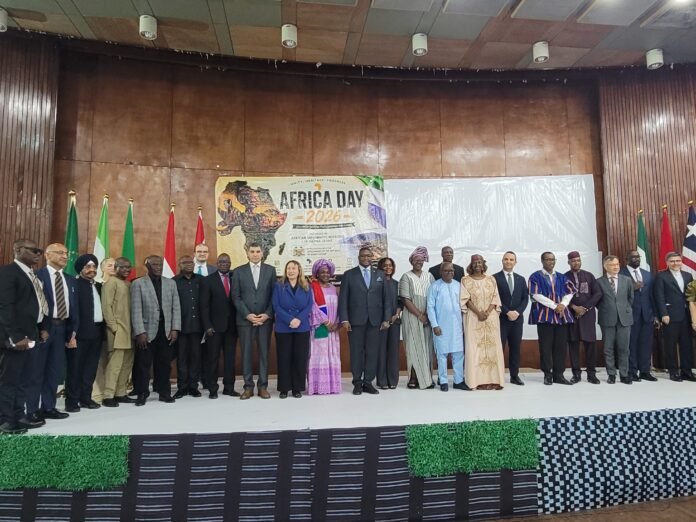 Dignitaries in formal attire pose on stage at Africa Day 2026, flags lined up behind them.