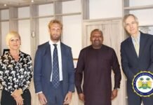 VP Engages German Ambassador, GIZ Country Director on Health Partnership, Receives Hamburg Conference Invitation Four professionals pose for a photo in an office-like setting: a woman in a black floral blouse on the left, two men in suits, and a man in traditional dark attire, with an official seal for the Office of the Vice President visible at the bottom-right.