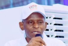 Alhaji Amadu Juldeh Sowe Rises from Local Baker to Industrial Powerhouse as New Flour Mill Boosts Sierra Leone’s Economy Speaker in a white polo and cap speaks into a handheld mic at a lectern decorated with blue and yellow ribbons (Life Flour logo on hat)