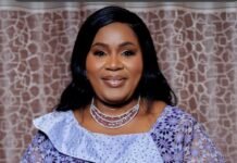 Hon. Rosemarie Bangura Elevates Sierra Leone on the Continental Stage Portrait of a smiling woman in a lavender lace dress with a silver choker necklace, standing before a patterned backdrop.
