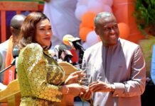 Pavifort Honoured for Excellence in Building Gambia’s First Data Centre Woman in a gold sequin dress hands a glass award to a smiling man at an outdoor press event with microphones nearby.
