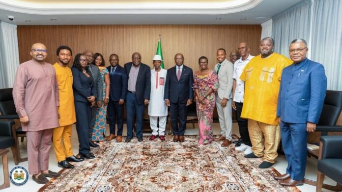 Group of dignitaries posing for a formal photo in a conference room, with the Nigerian flag in the background behind them.
