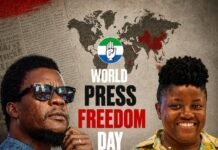 As SLAJ, Reporters Union React… Sierra Leone Drops Over 20 Places in 2026 Press Freedom Global Index Ranking, Faces Critical Test Two people stand side by side in front of a World Press Freedom Day poster, with a world map background and press-related props like a camera, notebook, and shackled documents to symbolize censorship.