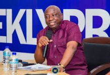 ONS Begins Probe Into Reported Cocaine Seizure Linked to Vessel From Freetown Smiling man in a maroon shirt speaks into a handheld microphone at a panel, seated at a table with papers and bottled water, against a blue backdrop.