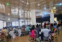 SLURC Concludes Urban SHADE Workshop, Calls for Coordinated Action Against Climate Threats in Informal Settlements Large hall filled with people seated at round tables, listening to a speaker on a stage at the front.
