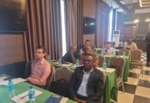 Woord en Daad, Solidaridad, World Vision & Cotton Tree Foundation Push for Stronger and Sustainable VSLAs in Sierra Leone Participants at a conference seated at tables with green tablecloths, water bottles and notebooks on them in a banquet-style room.