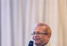 Ahead of Upcoming Fourth Forum Summit in New Delhi… India High Commission Hosts Strategic Briefing on India-Africa Business Dialogue & Exhibition 2026 Man in a light gray vest and dark shirt speaks into a handheld microphone at a wooden podium.