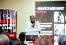 ‘ChopWin’ Online Casino Platform Officially Launched in Sierra Leone Man in a striped shirt speaks at a podium during a presentation, with banners and a large screen behind him.
